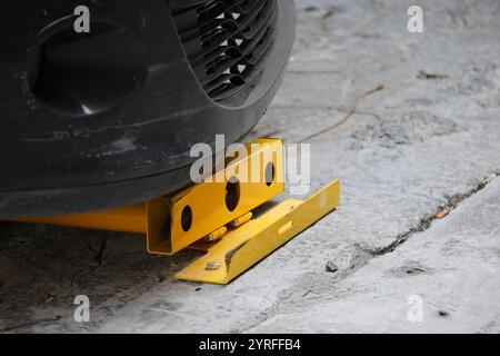 Gros plan d'une roue de voiture fixée avec un collier de roue jaune sur la chaussée Banque D'Images