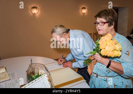 Un couple âgé signe des documents dans un bureau d'enregistrement en Russie, célébrant leur 50e anniversaire de mariage. La femme tient un bouquet de rose jaune Banque D'Images