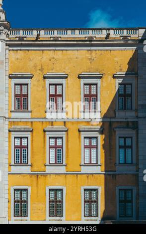Lumière du soleil illuminant la façade jaune du palais national de mafra au portugal avec un jeu captivant de lumière et d'ombre sur les fenêtres Banque D'Images