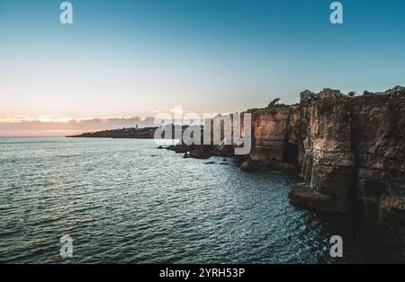 Les teintes chaudes du coucher de soleil peignent le ciel tandis que les falaises accidentées de boca do Inferno rencontrent la vaste étendue de l'océan atlantique, créant un coa à couper le souffle Banque D'Images