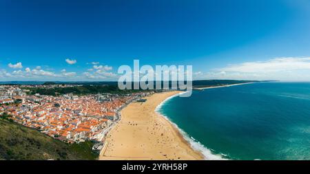 Sable doré et eaux bleues de praia de nazare, un charmant paysage urbain sous un ciel vibrant avec des nuages moelleux Banque D'Images