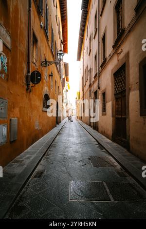 Deux touristes marchant dans une rue pavée étroite à florence, en italie, avec de hauts bâtiments de chaque côté, vers une lumière brillante à la fin de la s. Banque D'Images