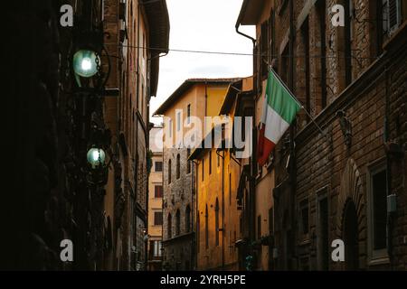 Lumière chaude du coucher de soleil illuminant les bâtiments colorés dans une rue étroite de florence, avec un drapeau italien suspendu à un bâtiment et des lampes vintage Banque D'Images