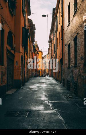 Rue humide à bologne, italie avec de vieux bâtiments, des graffitis et des flaques d'eau, reflétant l'histoire européenne et la culture italienne Banque D'Images