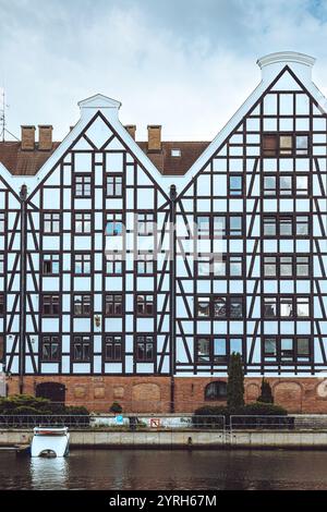 Des bâtiments à ossature de bois blanc et noir se dressent le long de la rivière Motlawa à gdansk, en pologne, mettant en valeur l'architecture traditionnelle et reflétant dans le cal Banque D'Images