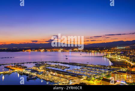 Paysage urbain de roses, espagne, avec son port et ses bateaux reflétant dans la mer, illuminé par la lumière chaude du soleil couchant sur les montagnes Banque D'Images