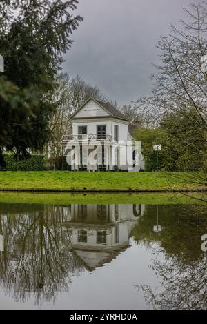 Une charmante maison blanche labellisée 'de Wildkamp' se dresse près d'un étang calme, reflétant parfaitement dans l'eau. Entouré d'arbres et de verdure, le couvert Banque D'Images