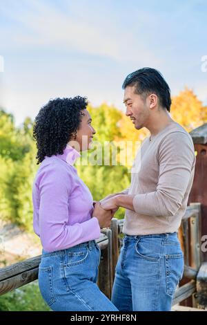 Un couple se tient proche, souriant et se tenant la main, profitant d'une journée ensoleillée dans un parc la toile de fond naturelle présente des arbres verdoyants, créant un cadre serein et Banque D'Images