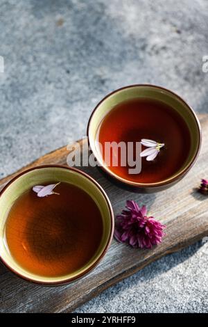Deux tasses à thé élégantes remplies de thé riche et de couleur ambre sont ornées de délicats pétales de fleurs la scène repose sur une surface en bois rustique, améliorant Banque D'Images