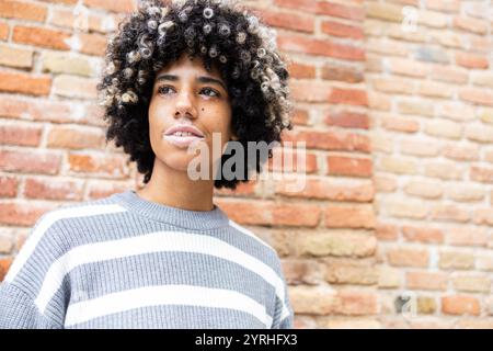 Une femme de race mixte avec vitiligo se détend sur un campus universitaire, debout près d'un mur de briques sa tenue décontractée et son expression sereine illustrent un peacefu Banque D'Images