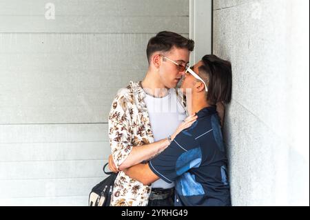 Un moment tendre capturé comme un jeune couple gay partage un baiser passionné contre un mur de béton dans un cadre urbain, mettant en valeur des styles contemporains et Banque D'Images