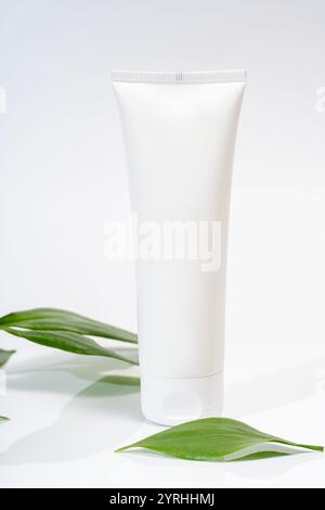 Tube cosmétique blanc simple avec des feuilles vertes, placé sur un fond clair et propre parfait pour mettre en valeur les soins de la peau, la lotion, la crème ou b écologique Banque D'Images