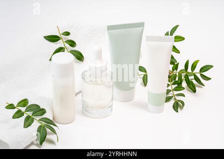 Un arrangement serein de bouteilles cosmétiques avec une serviette blanche et des branches vertes idéal pour le spa, les soins de la peau et les thèmes de beauté naturelle minimaliste et frais Banque D'Images