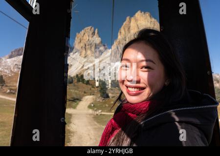 Une femme asiatique souriante profite d'un trajet en téléphérique à Forcella del Sassolungo, en Italie. Les majestueux sommets des Dolomites créent une superbe toile de fond sous un clair Banque D'Images