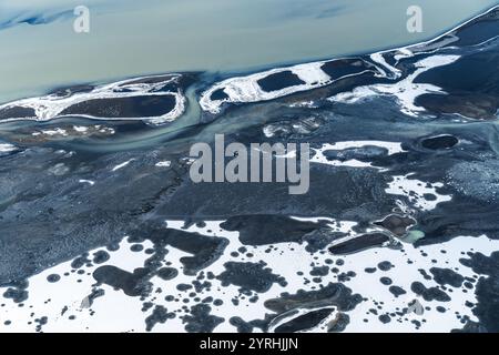 La prise de vue aérienne de la côte sud de l'Islande illustre le contraste saisissant entre les sables volcaniques sombres et les paysages enneigés, créant ainsi une toile de fond unique Banque D'Images