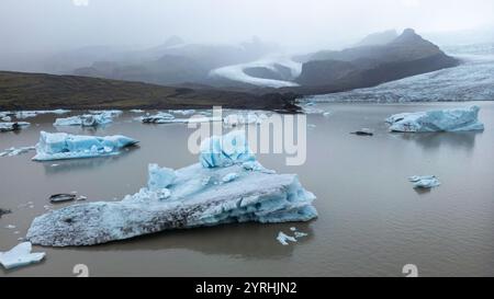 Paysage glaciaire impressionnant avec de vastes icebergs flottant dans un lagon serein du parc national de Vatnajokull, Islande Misty Mountains complètent le Banque D'Images