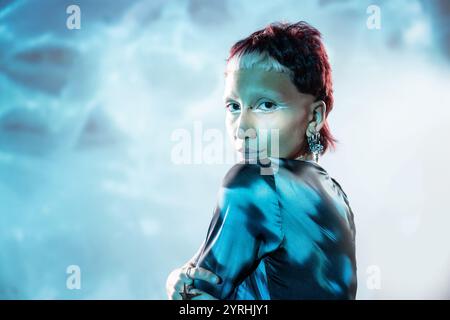 Femme regardant la caméra dépeignant un personnage futuriste, stylisé avec un maquillage des yeux frappant et des boucles d'oreilles edgy, placé sur un fond éthérée en sucre Banque D'Images