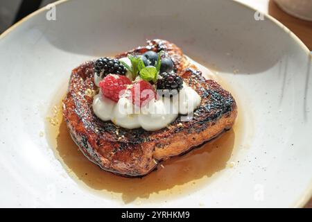 Une appétissante portion de pain grillé garnie de framboises fraîches, de mûres et de myrtilles, accompagnée d'une cuillère de crème fouettée sur un filet Banque D'Images