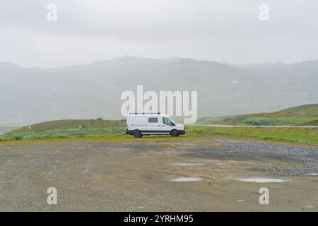 Un paysage serein en Laponie suédoise met en valeur un camping-car blanc garé au milieu d'une vaste verdure et de montagnes brumeuses, offrant un sentiment d'aventure et Banque D'Images