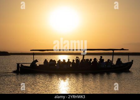 Un grand bateau rempli de gens regardant le magnifique coucher de soleil. Les teintes jaunes rayonnantes chaudes du soleil couchant créent un beau contraste avec le dar Banque D'Images