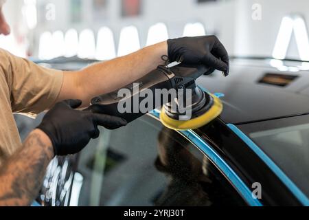 Homme professionnel polissant la voiture noire et enlevant les rayures dans le centre de détail Banque D'Images
