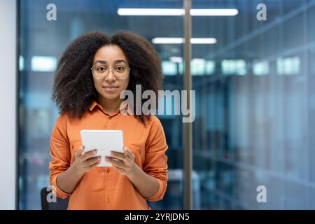 Jeune femme d'affaires utilisant une tablette dans un bureau moderne. Cette professionnelle férue de technologie s'engage avec confiance dans l'appareil numérique, mettant en valeur la polyvalence et l'innovation dans son travail. Banque D'Images