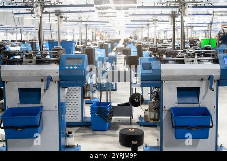 Vue de machines automatisées de fabrication de textiles dans une usine, avec des bobines de fil blanc prêtes pour le traitement. Banque D'Images