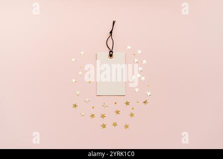 Étiquette de prix vierge, étiquette blanche avec une ficelle noire est placée au centre, entourée de décorations en forme d'étoile dorée sur un fond beige doux. Haut v Banque D'Images