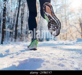 Chaussures de course semelle gros plan image des pieds de jogging d'hiver dans les baskets de course sur le chemin enneigé du parc pendant la journée ensoleillée. Vue arrière de la semelle. Banque D'Images