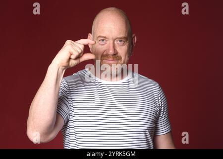 Homme qui montre avec ses doigts qu'il est petit sur fond rouge Banque D'Images