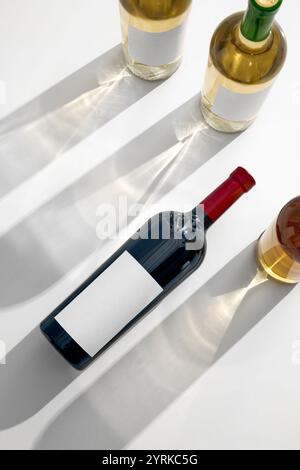 Perspective à plat de bouteille de vin rouge entourée de bouteilles de vin blanc, ombres de bouteilles s'étendant sur la surface blanche dans des motifs élégants Banque D'Images