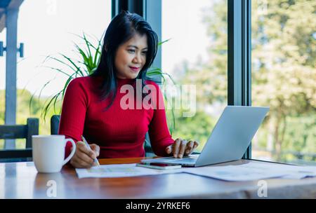 Femme d'affaires tenant un stylo et utiliser un ordinateur portable tout en travaillant au bureau, gros plan les mains de la femme utilisent le stylo pour analyser les graphiques et les données commerciales. Banque D'Images