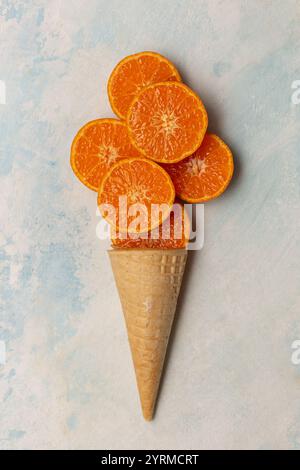 Cône gaufré avec tranches de mandarine tranchées sur un fond bleu, vue de dessus Banque D'Images