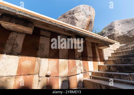 Des marches de pierre conduisent devant un ancien temple au site historique de Shravanabelagola sur fond de grands rochers. Banque D'Images