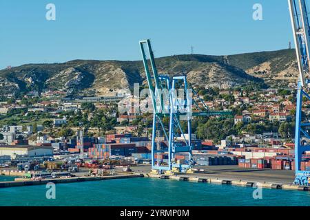 L'image capture une grue imposante au port de Marseille, avec des conteneurs maritimes colorés et un paysage urbain en arrière-plan, mettant en évidence le port Banque D'Images