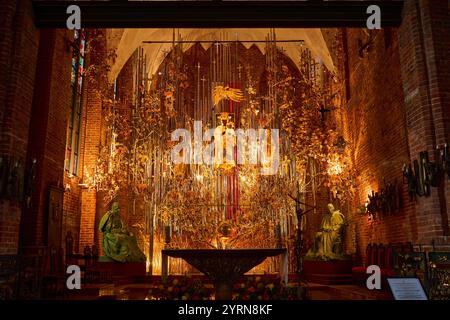Un intérieur orné d'une église de Gdansk avec un autel magnifique orné de sculptures en ambre doré, de décorations florales et de statues, illuminé par Banque D'Images