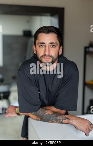 Bel homme avec les cheveux et la barbe en T-shirt noir se tient à la réception dans le salon de coiffure Banque D'Images