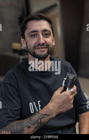 Coiffeur professionnel masculin avec tondeuse à cheveux assis dans la chaise dans le salon de coiffure Banque D'Images