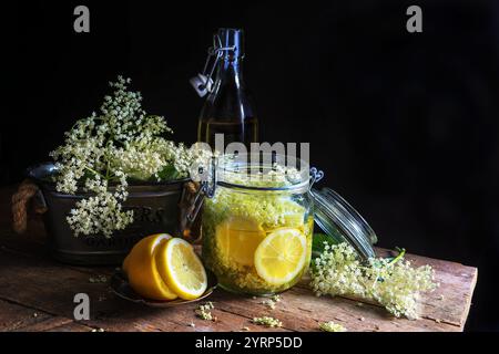 Sirop de fleur de sureau fait maison en pot et fleurs de sureau sur table en bois - photographie sombre et sombre Banque D'Images