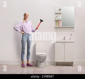 Femme souriante debout dans une salle de bain et tenant un piston de toilette Banque D'Images