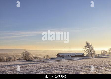 Ferme à la campagne avec une belle vue dans une vallée avec des éoliennes à l'horizon sur une journée d'hiver froide et ensoleillée avec de la neige et du givre, S. Banque D'Images