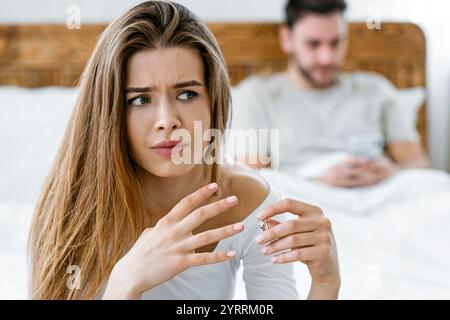 Femme triste enlève son alliance de près, mari tapant au téléphone dans le lit Banque D'Images