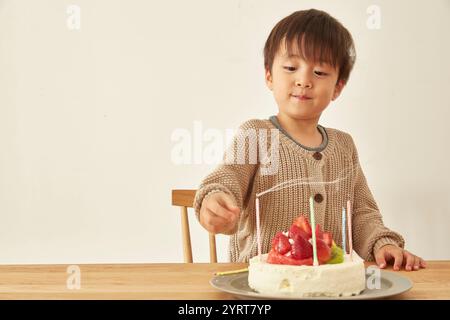 Garçon semblant satisfait après avoir soufflé les bougies sur le gâteau de célébration. Banque D'Images