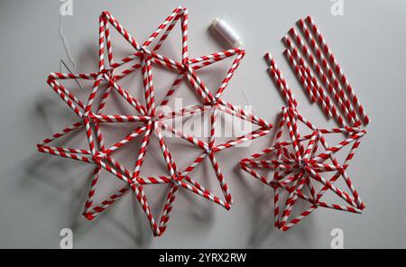 Ensemble d'étoiles faites à la main en rayure rouge et blanche. Forme différente. Chaotiquement placé sur fond blanc. Aiguille, fil blanc, pailles en papier pour boissons Banque D'Images