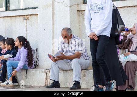 Un homme plus âgé lisant un livre assis sur une corniche en béton dans un espace public, Alger, Algérie. Banque D'Images