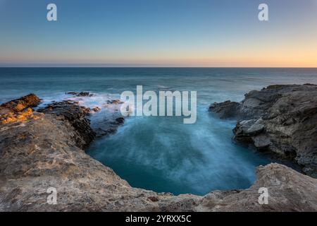 Les vagues s'écrasent doucement contre les falaises rocheuses de Leo Carrillo State Beach alors que le soleil se couche, créant une vue sereine et pittoresque sur la côte. Banque D'Images