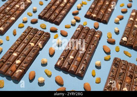 Barres de chocolat noisettes parmi les noix dispersées et les raisins secs sur un fond bleu. Banque D'Images