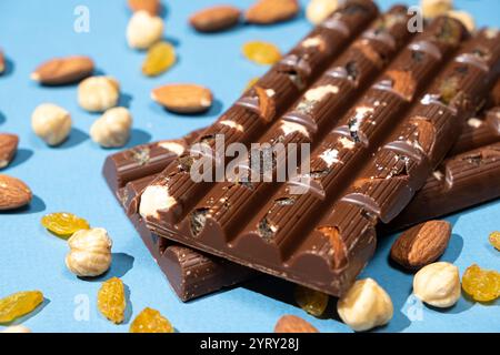 Barres de chocolat noisettes parmi les noix dispersées et les raisins secs sur un fond bleu. Banque D'Images