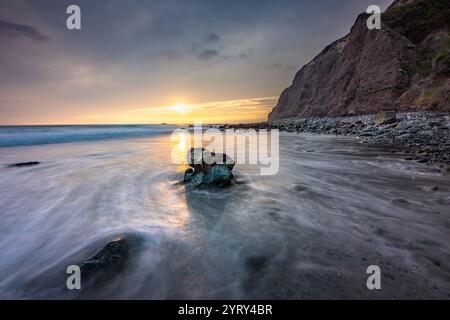 Les vagues tapent doucement contre le rivage alors que le soleil se couche derrière les falaises de Dana point. La scène tranquille capture la beauté et la sérénité de la nature. Banque D'Images