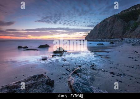 Les vagues tapent doucement contre la rive rocheuse alors que le soleil se couche derrière les falaises de Dana Cove, en Californie du Sud, créant une atmosphère sereine. Banque D'Images